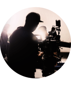 Black and white image. Shows a man behind a camera with a spotlight.